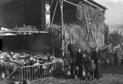 Capellans i nens al costat d'un estable amb xais i un paller. 1940-1950